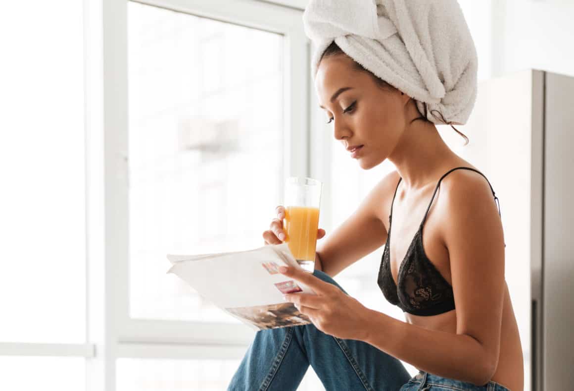 woman-wearing-jeans-with-a-towel-wrap-reading-a-newspaper-drinking-orange-juice
