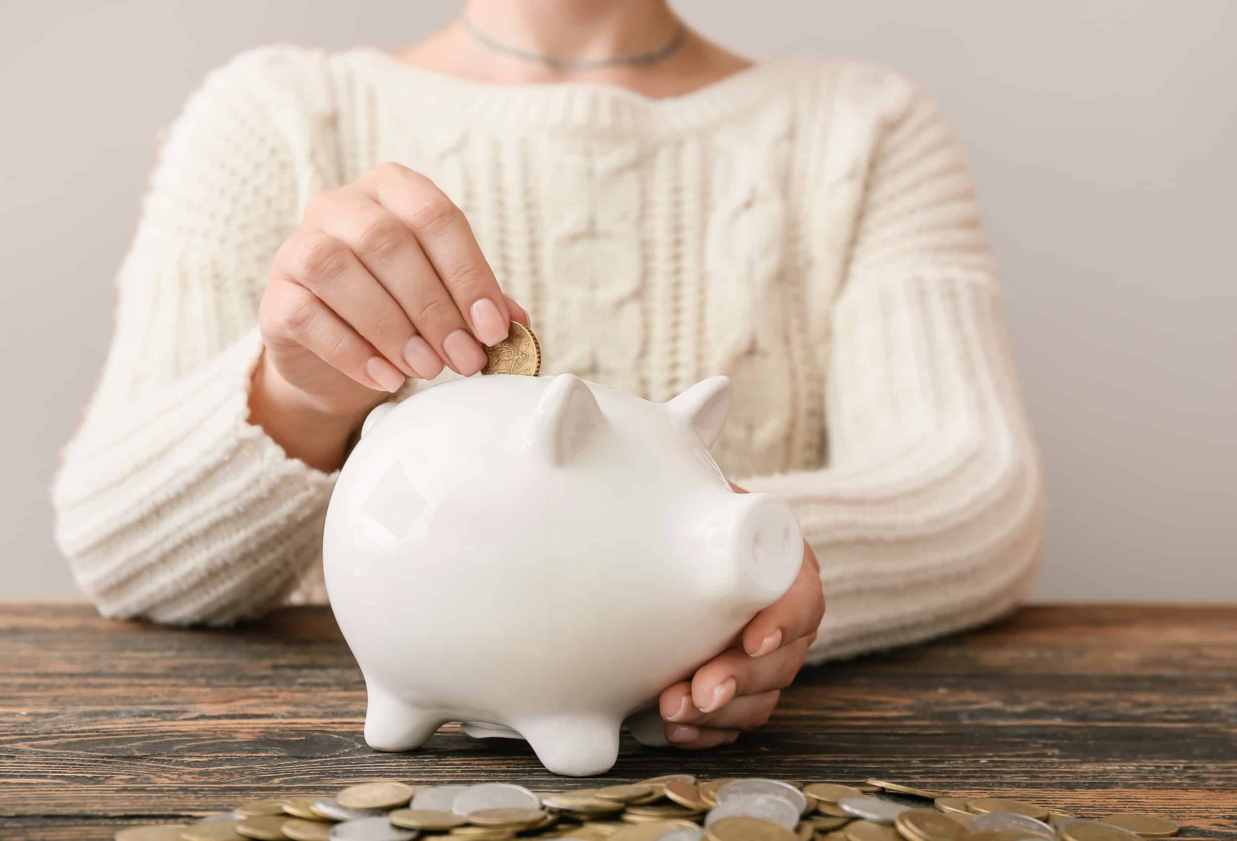 woman-in-cream-sweater-putting-coins-in-a-piggy-bank