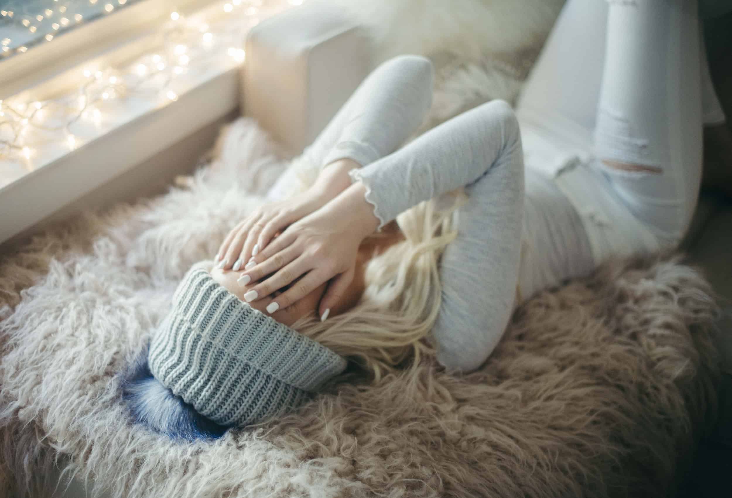 woman-in-comfortable-warm-clothes-laying-in-bed-covering-face