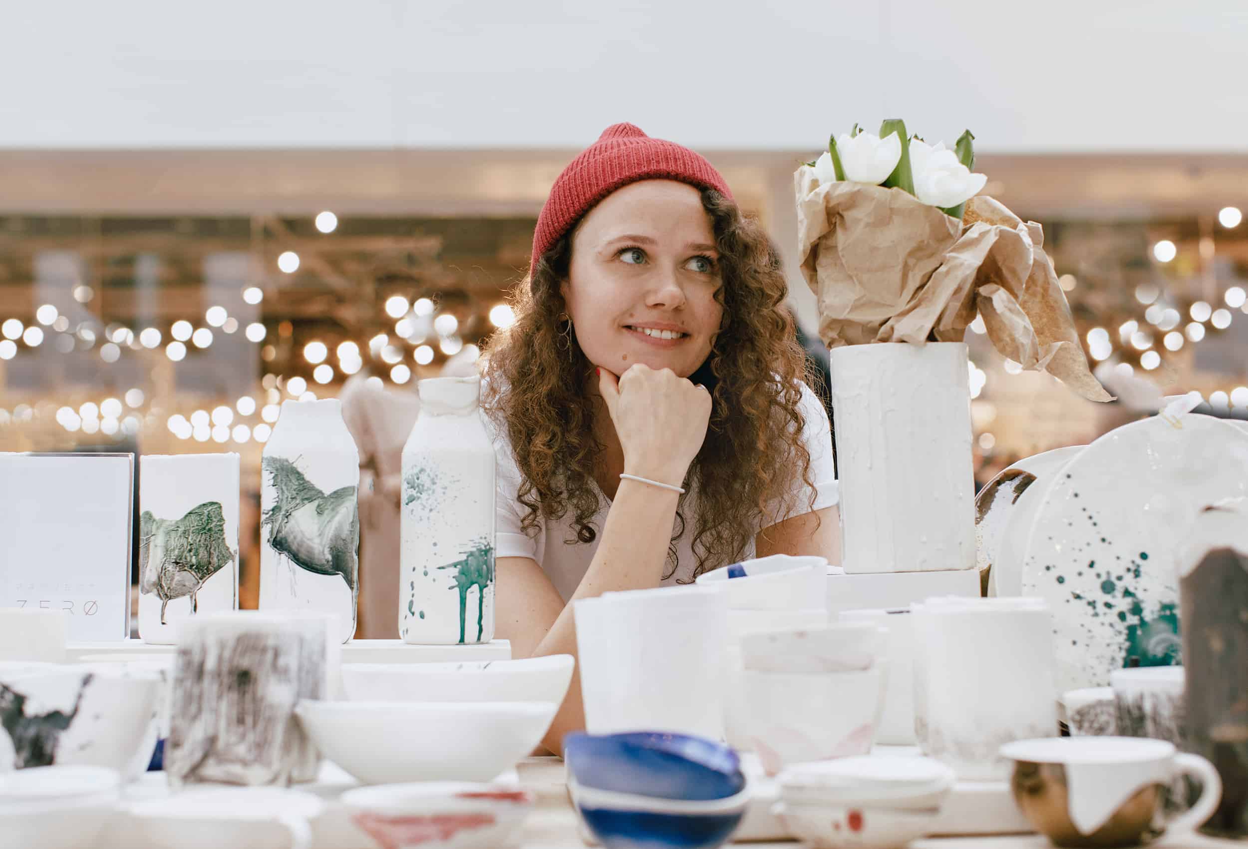 woman-wearing-a-red-beanie-daydreaming-surrounded-by-ceramics-and-art