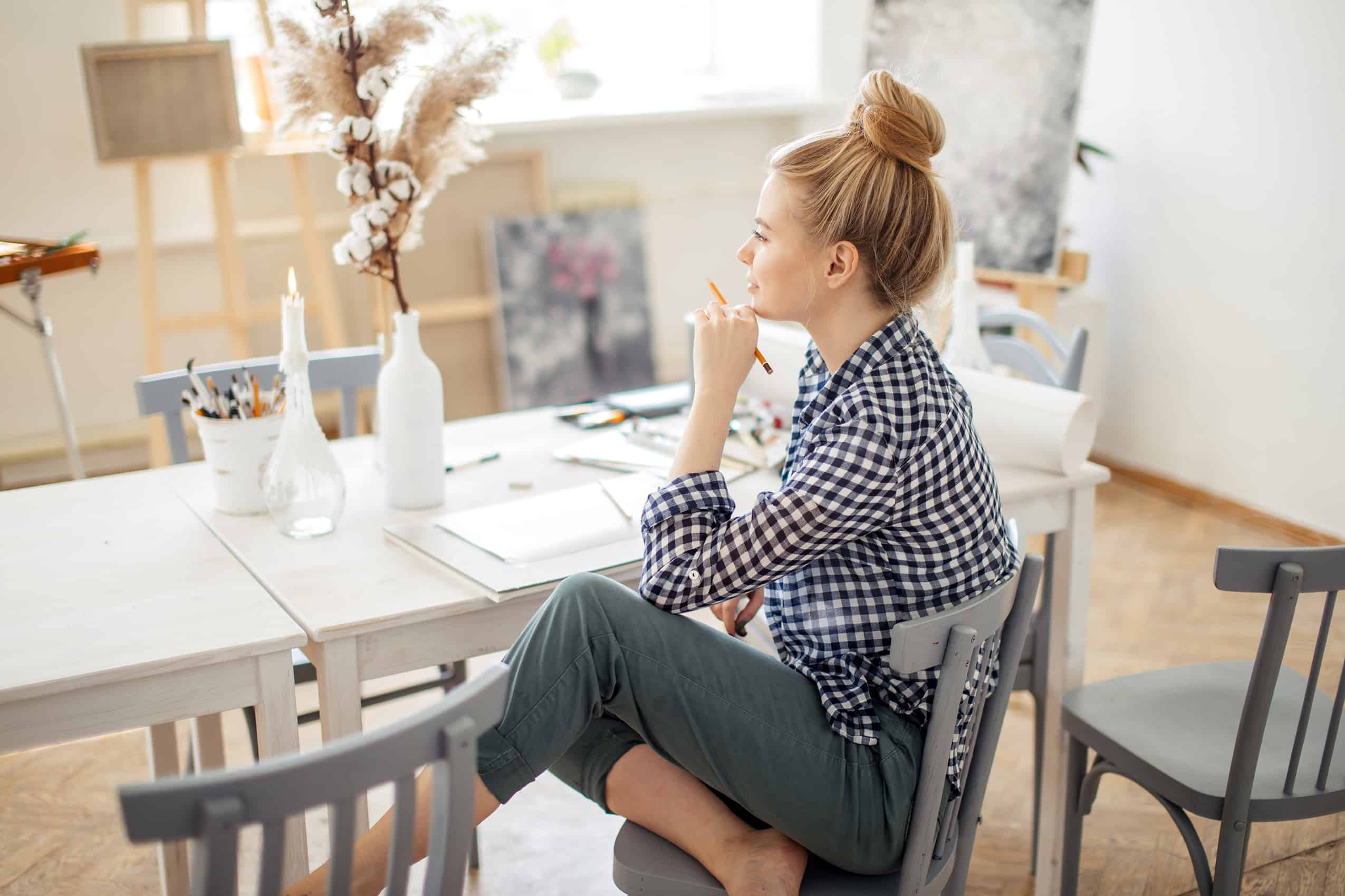 woman-siting-at-table-thinking-and-journaling-surrounded-by-art
