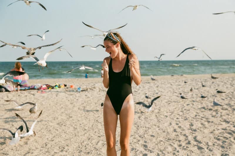 young woman in bathing suit on beach happy with birds self love