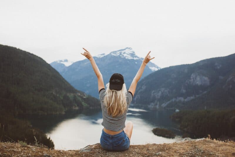 young woman sitting with arms in air freedom in nature self love