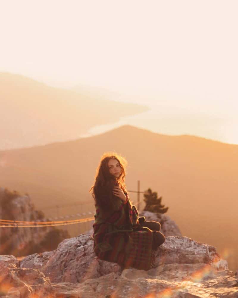 woman-curly-hair-sitting-on-rock-in-nature