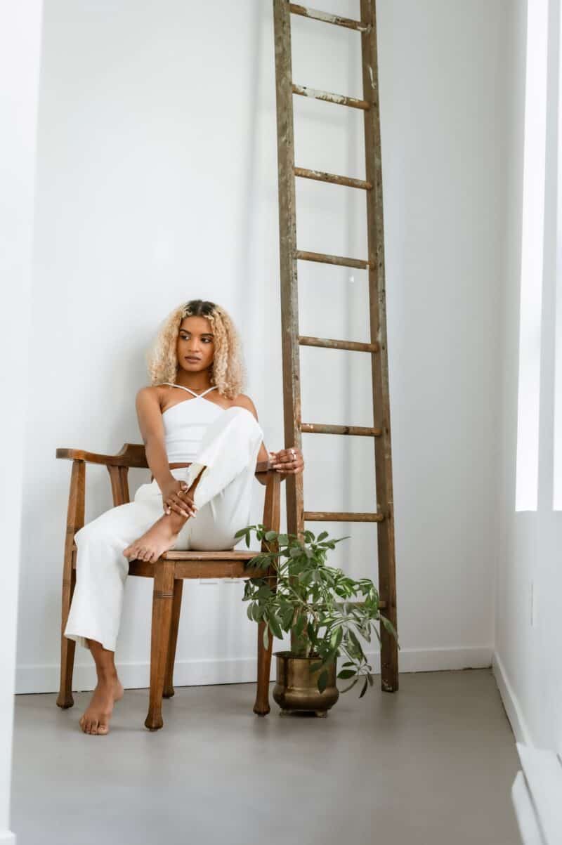 woman-in -white-sitting-on-chair-next-to-plant-and-ladder