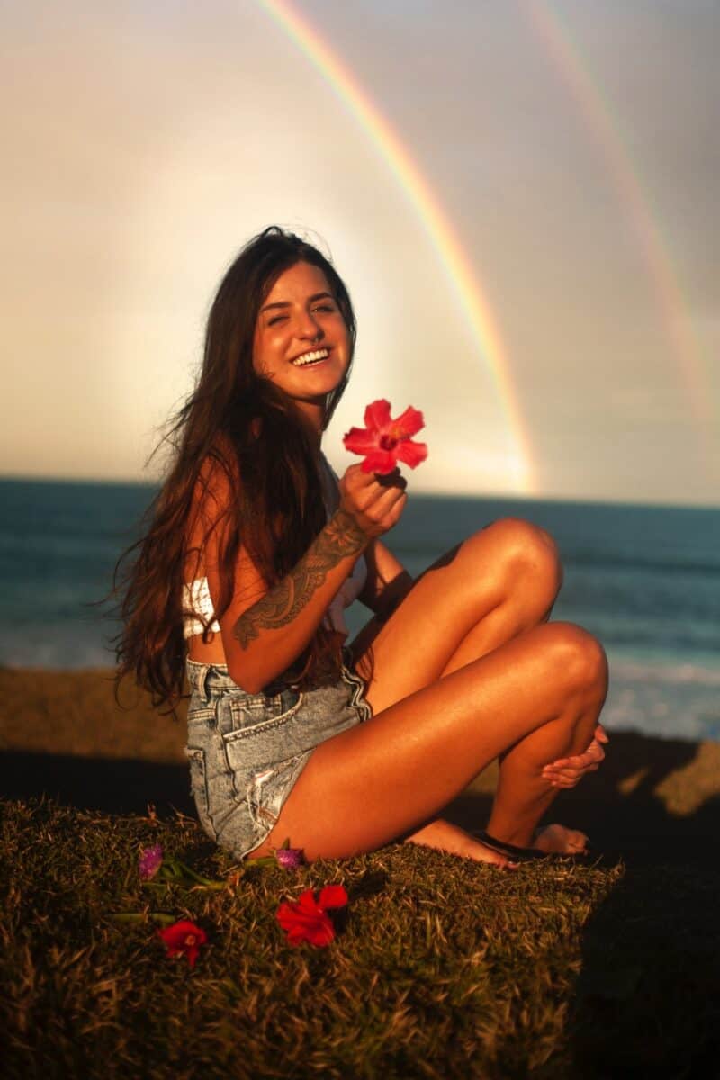 pretty-woman-long-hair-holding-red-flower-smiling-on-beach-rainbow