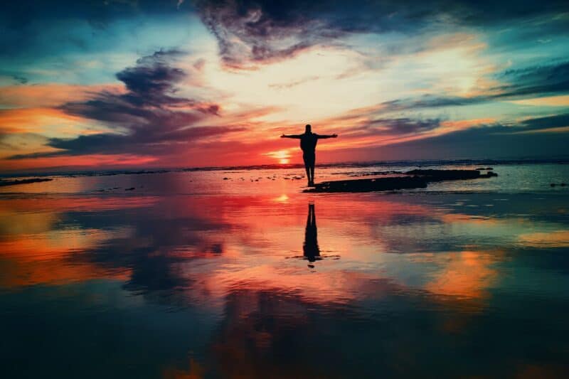 man-standing-with-arms-wide-open-on-beach-with-magnetic-sky-