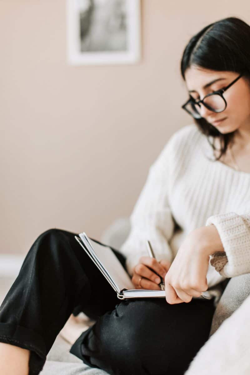 woman-with-black-hair-glasses-writing-in-manifestation-journal